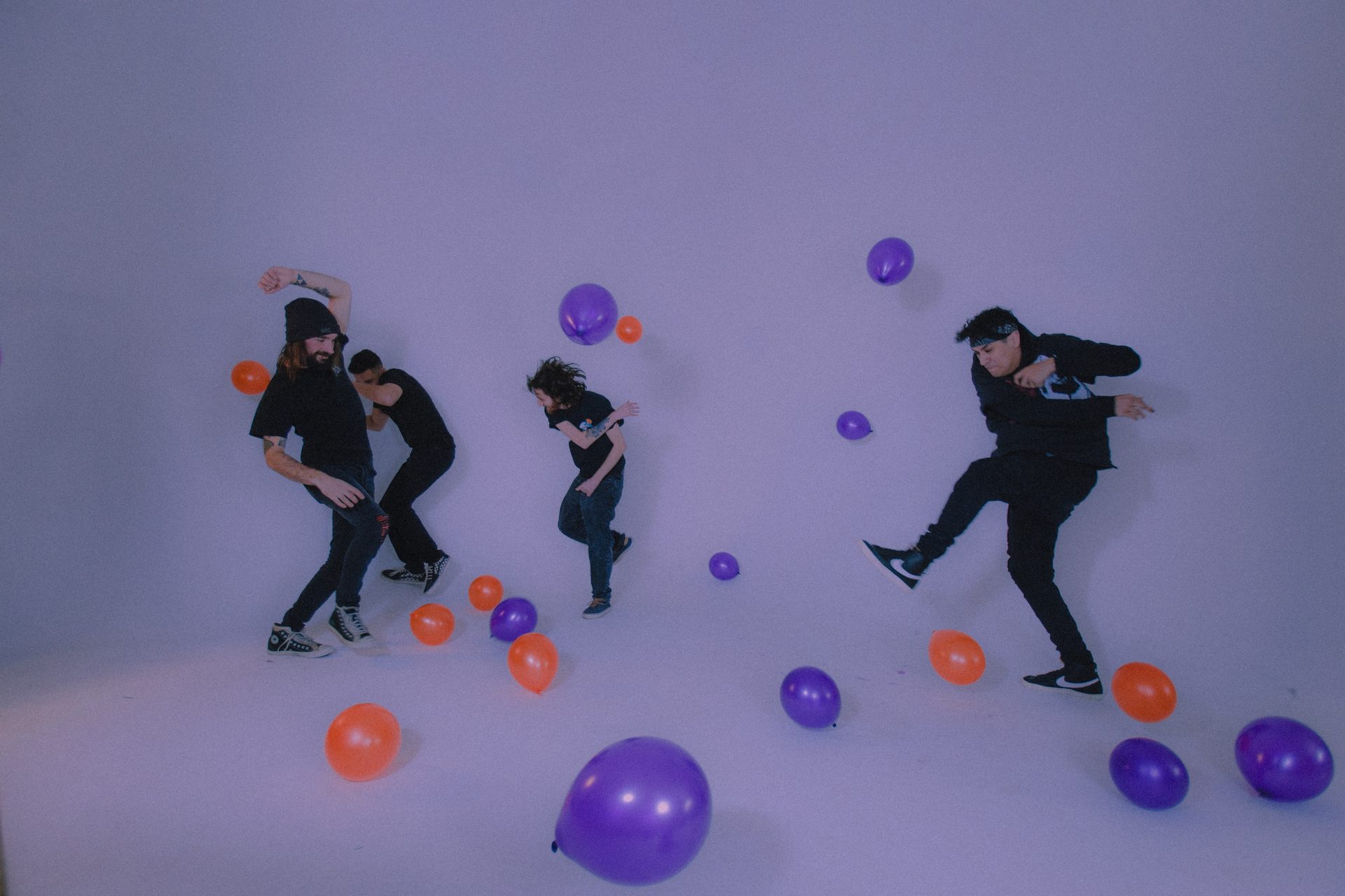 The four members of Back From Nothing jumping among purple and orange balloons in a white studio